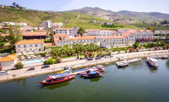 a picturesque riverside village with houses , trees , and boats on the water , set against a backdrop of mountains at The Vintage House - Douro
