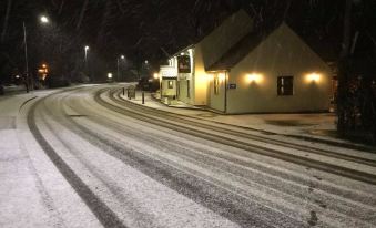 a snow - covered street at night with buildings lit up , creating a serene atmosphere under the dark sky at The Black Horse Inn