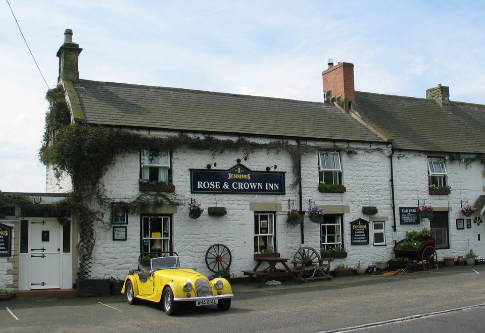 "a yellow car is parked in front of a white building with the sign "" rose and crown inn .""." at Rose & Crown