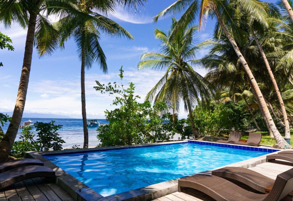 a large pool surrounded by palm trees , with a view of the ocean in the background at Sali Bay Resort