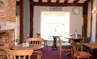 a dining area with wooden tables and chairs , a clock on the wall , and a window at Limes Hotel