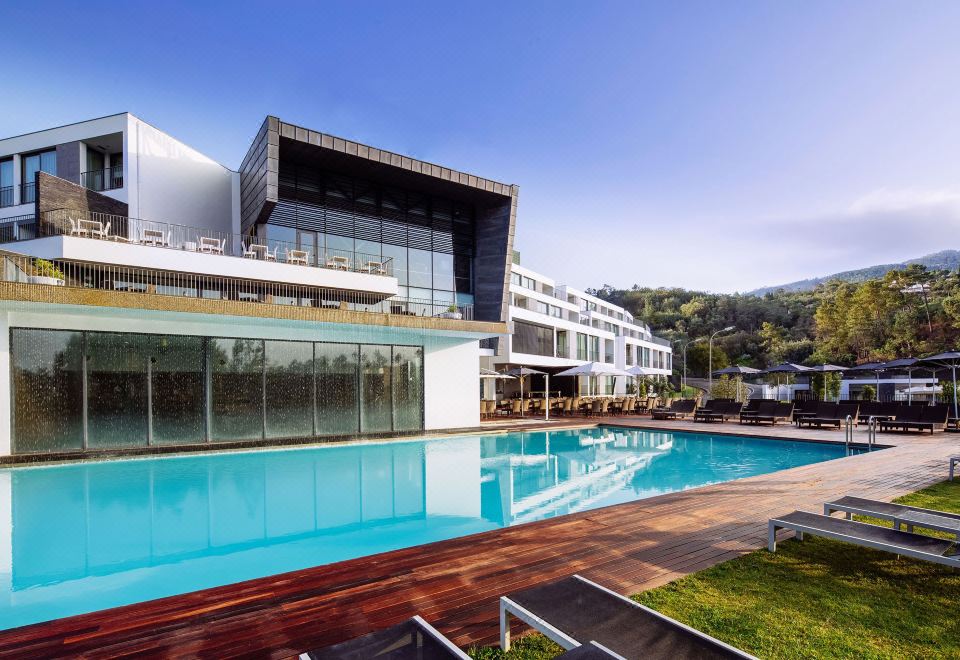 a modern building with a large pool and lounge chairs is surrounded by greenery and mountains at Monchique Resort & Spa