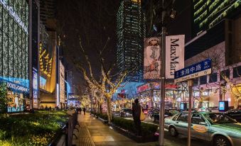 A city street at night with pedestrians and cars on the sidewalk in front at Huaihai Mansion