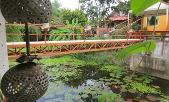 a wooden bridge with a red railing , leading to a small pond filled with lily pads and pink flowers at Baan Ton Nam Resort SuanPhueng