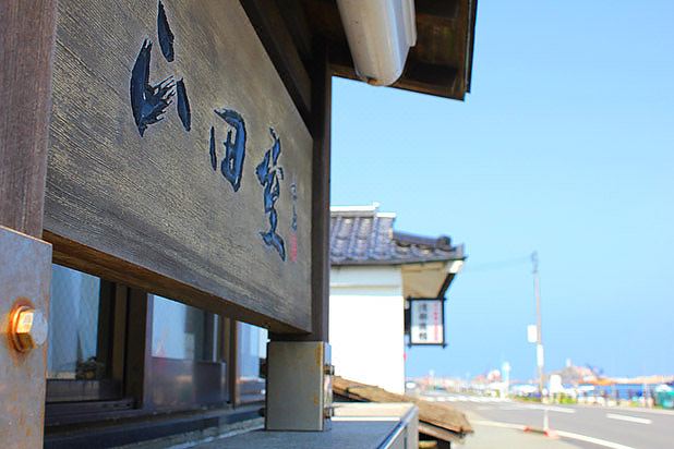 a wooden building with blue chinese characters on it , overlooking a body of water and a bridge at Yamadaya