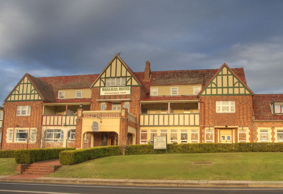 a large , red brick building with multiple balconies and a green lawn in front of it at Wallacia Hotel