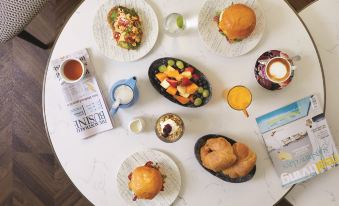 a table is set with a variety of food items including sandwiches , fruits , and a newspaper at Vibe Hotel Sydney