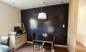 a dining room with a black brick wall , a dining table with two chairs , and a kitchen area at Best East