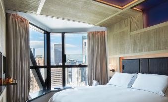 The hotel features a bedroom with expansive windows and floor-to-ceiling glass that offers a panoramic view of the city at The Emperor Hotel