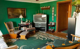 a living room with green walls , a wooden floor , and furniture including a television , chairs , and a coffee table at Lamplight Inn