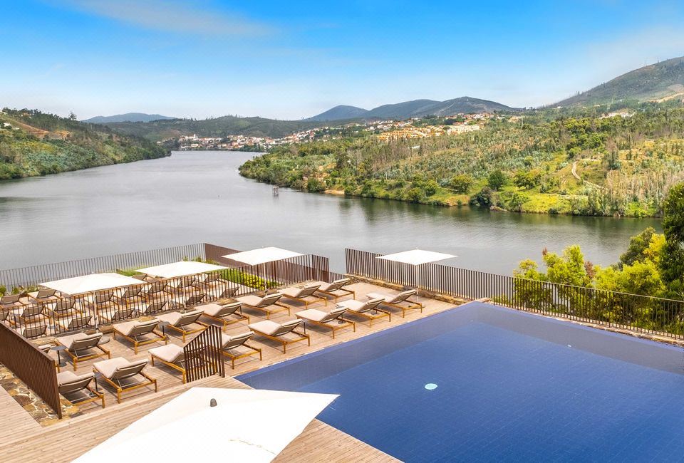 a large swimming pool is surrounded by lounge chairs and umbrellas , with a river visible in the background at Octant Douro