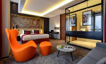 a modern hotel room with an orange couch , a dining table , and a bed in the background at Grand Hotel la Cloche Dijon - MGallery