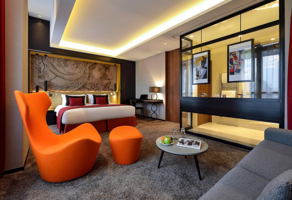 a modern hotel room with an orange couch , a dining table , and a bed in the background at Grand Hôtel la Cloche Dijon - MGallery