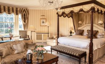 a luxurious bedroom with a large bed , a chaise lounge , and a fireplace , all decorated in shades of white and beige at Lucknam Park Hotel