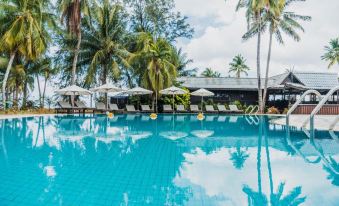 a large swimming pool surrounded by palm trees , with lounge chairs and umbrellas placed around it at Berjaya Tioman Resort