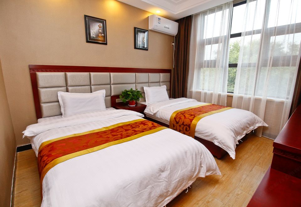 There are two beds in the bedroom, positioned next to each other, with a large window on one side at Famen Temple Hotel