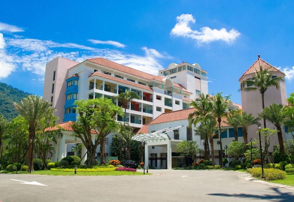 a large white building with multiple floors and balconies , surrounded by trees and a parking lot at Hotel Cham Cham