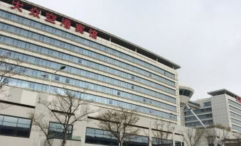 Across the street, there is an office building in the background, a large white building on the right side, and a hotel with a glass facade and a sign on top, with a few cars parked in front at Da Zhong Airport Hotel