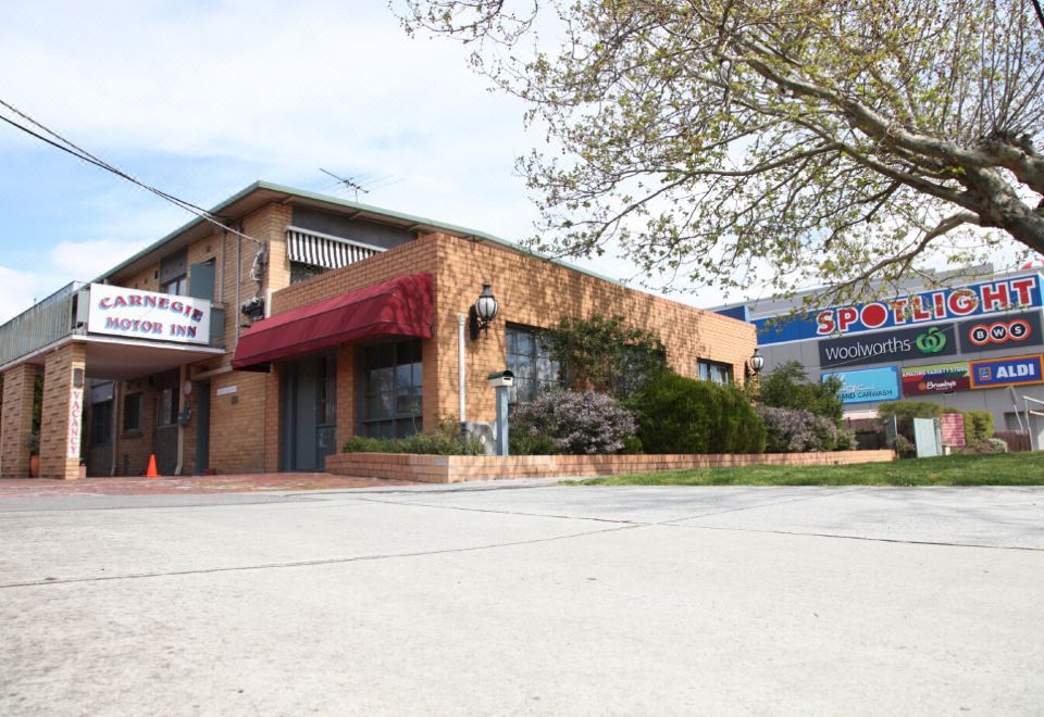 "a brick building with a red awning and a sign that reads "" kiis pizza "" in front of it" at Carnegie Motor Inn