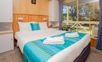 a well - arranged hotel room with a large bed , white linens , and blue accents , near a window that offers a view of the at Shepparton Holiday Park and Village