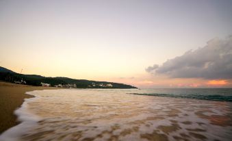 a serene beach scene with a body of water and the sun setting in the background at Red House