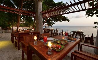 a wooden dining table with a plate of food , surrounded by chairs and a view of the ocean at Sai Daeng Resort