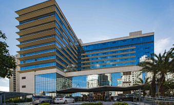 A large building with parked cars in front and its glass facade reflecting the surroundings at Hainan Grand Hotel
