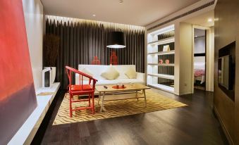 A modern living room features white walls, hardwood floors, and a red accent wall with black accents at Metropolo Dahua Hotel Shanghai