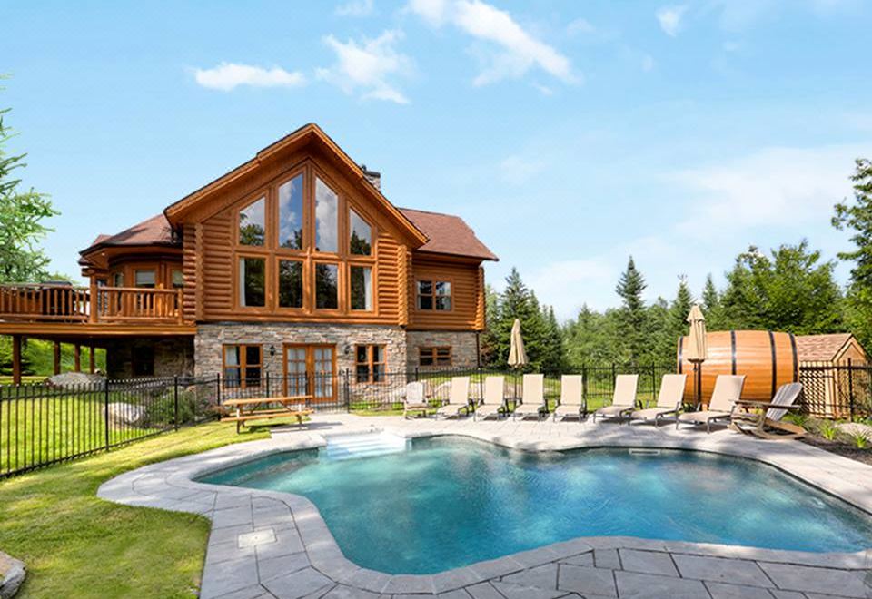 a large wooden house with a swimming pool in front of it , surrounded by lush greenery at Fiddler Lake Resort