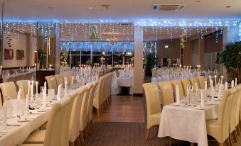 a large , well - lit banquet hall with multiple tables set for dining , each table covered in white tablecloths and decorated with christmas at Majestic Hotel