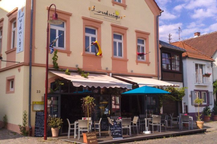 a restaurant with outdoor seating and umbrellas on the street , set against a backdrop of buildings at LUDWIGS