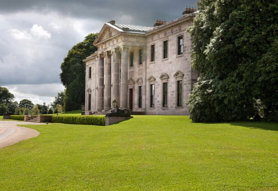 a large white building with columns is surrounded by a lush green lawn and trees at Ballyfin Demesne