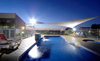 an outdoor swimming pool surrounded by a patio area , with lounge chairs and umbrellas placed around the pool at Quest Williamstown North