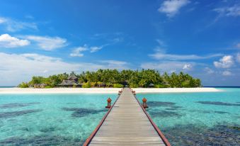 a wooden pier extends into the ocean with a clear blue sky and tropical trees in the background at Banyan Tree Vabbinfaru