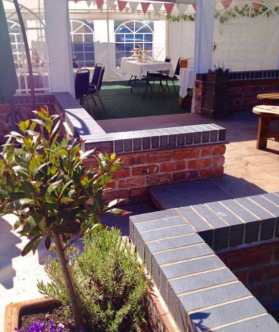 a courtyard with brick benches , potted plants , and tables under a glass roof , surrounded by a white building at St Quintin Arms