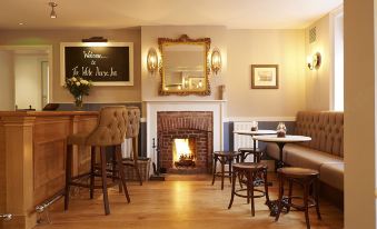 a cozy living room with a fireplace , bar area , and dining table , decorated with furniture and artwork at The White Horse Inn