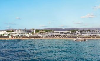 a large hotel situated on the beach , with clear blue water and a beautiful view of the ocean at Grecotel Lux.ME White Palace
