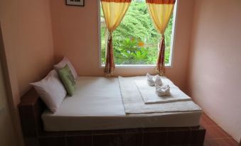 a bed with a white sheet and two pillows is situated next to a window at Baan Ton Nam Resort SuanPhueng