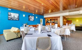 a well - lit dining room with white tables and chairs arranged for a large group of people at Riverfront Motel & Villas