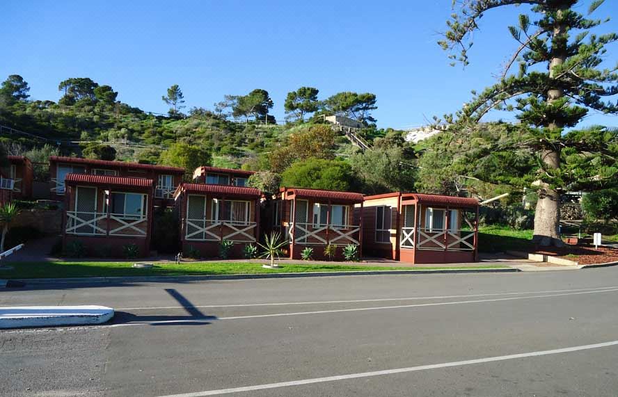 a row of red and white houses situated on a street with trees in the background at Brighton Beachfront Holiday Park Adelaide