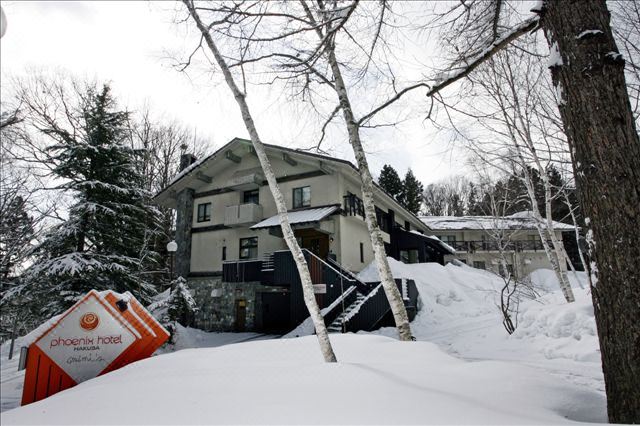 a snow - covered house with a red truck parked in front of it , surrounded by trees and covered in snow at Phoenix Hotel by Hakuba Hotel Group