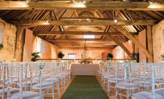 a wedding ceremony taking place in a barn , with rows of white chairs arranged for guests at Brasteds