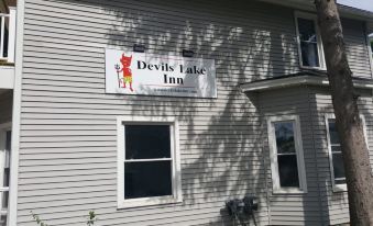 "a white building with a sign that reads "" devils lake inn "" prominently displayed on the front of the building" at Devils Lake Inn