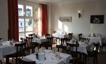 a well - lit restaurant with multiple dining tables and chairs arranged in a dining room , ready for guests at Falkensee