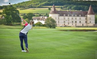 a woman is swinging a golf club on a golf course , with a large building in the background at Hotel Golf Chateau de Chailly