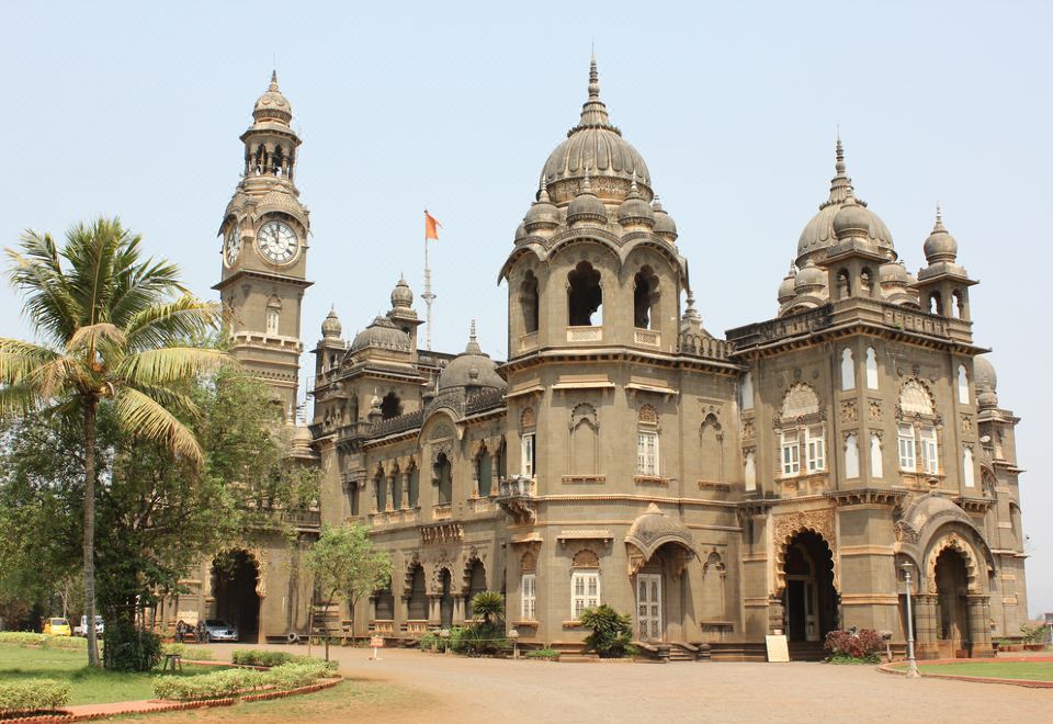 a large , ornate building with a clock tower and a sign on the front , surrounded by a grassy area at Hotel Rajlaxmi Grand