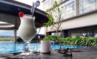 a glass of milk with a cherry and a spoon is placed on a table next to a pool at ASTON Purwokerto Hotel & Convention Center