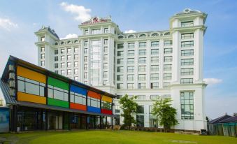 a large white hotel building with a colorful facade and a grassy courtyard in front at Westlake Hotel & Resort Vinh Phuc