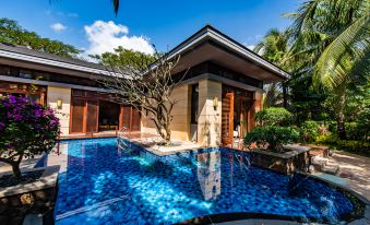 a large , blue pool is surrounded by a tropical setting with palm trees and a house at Sanya Haitang Bay Island Villa (International Duty Free City Branch)