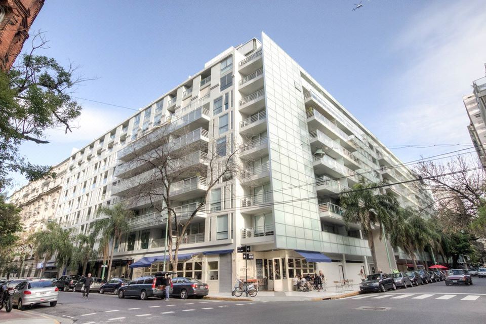 a modern building with a blue awning is situated on a street corner with parked cars at Kos Pilar Hotel